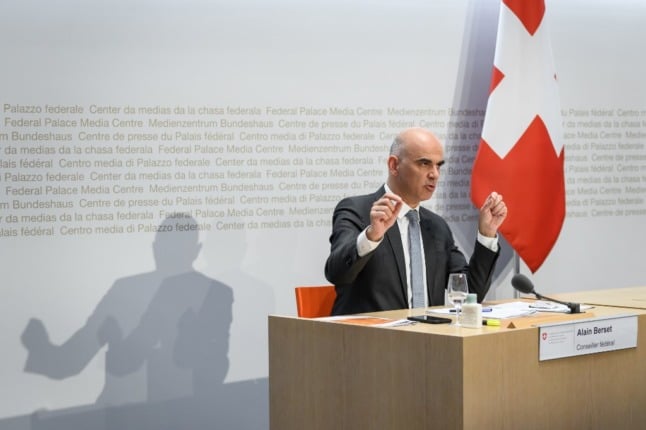Swiss Interior and Health Minister Alain Berset sitting next to a Swiss flag
