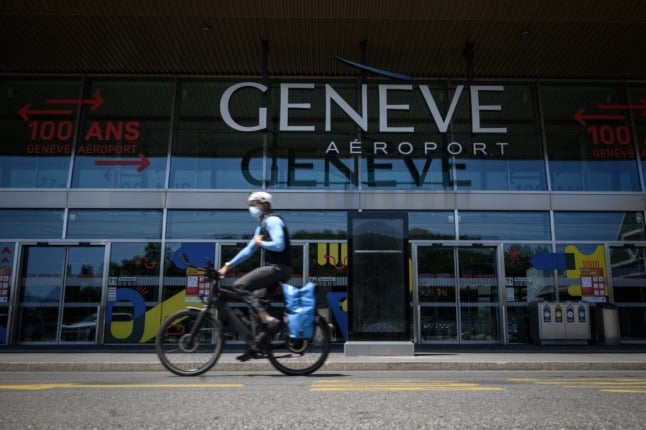 A man wearing a protective face mask rides his bicycle past the entrance of Geneva Airport.