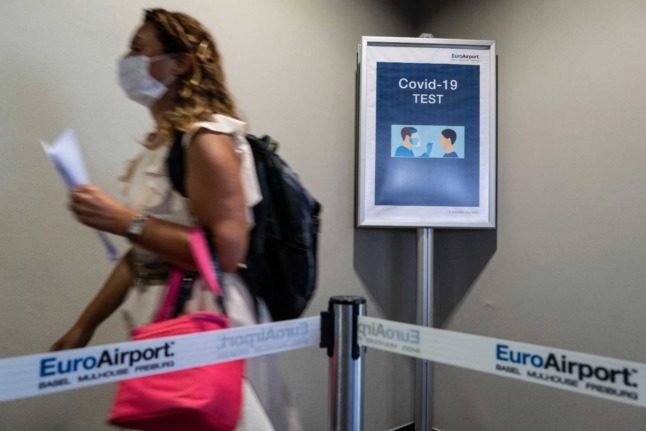 A person in a mask walks past a sign at Basel Airport