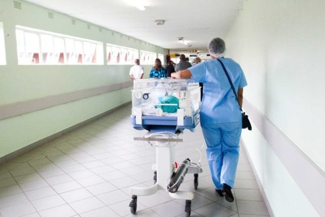 A nurse wheels a person in a hospital bed down a corridor 